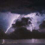 Lightning striking near a house at night, illustrating power surge damage and homeowners insurance coverage