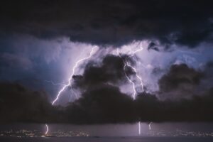 Lightning striking near a house at night, illustrating power surge damage and homeowners insurance coverage