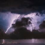 Lightning striking near a house at night, illustrating homeowners insurance power surge coverage