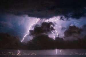Lightning striking near a house at night, illustrating homeowners insurance power surge coverage